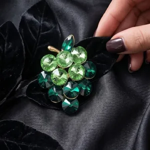 Elegant grape brooch with green and dark emerald crystals on dark silk background