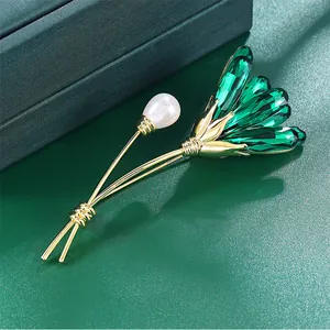 Close-up of elegant green crystal and pearl floral brooch with 14K gold-plated brass frame.