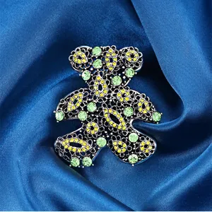 Detailed view of a hollow teddy bear brooch with green and yellow crystals on blue silk fabric