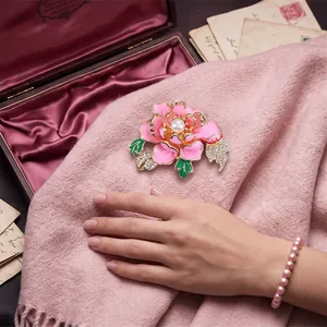 Elegante spilla a fiore di peonia rosa con strass e perla su morbido tessuto rosa.