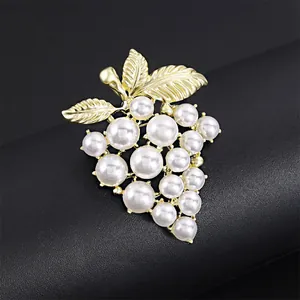 Makroaufnahme einer eleganten Traubenbrosche mit weißen Perlen und Goldblättern.