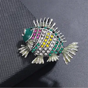 Detail einer bunten Fischbrosche mit glänzenden Strasssteinen und Emaille auf dunklem Grund.