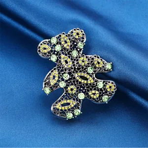 Detailed macro shot of a hollow teddy bear brooch with green and yellow crystals.