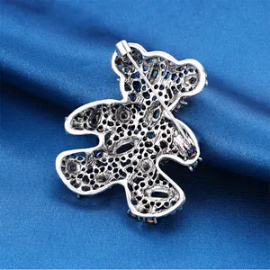 Back view of silver hollow teddy bear brooch with safety pin clasp on blue silk fabric