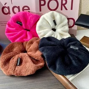 Close-up of plush oversized scrunchies in pink, white, brown and black velvet textures.