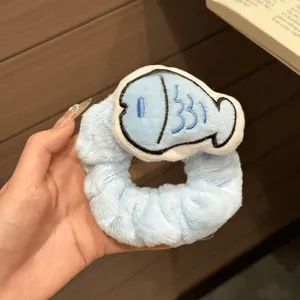 Close-up of a plush blue hair scrunchie with a cute cartoon fish embroidery details.