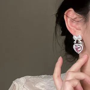 Detailed view of exquisite pink heart zircon earring with silver bow on model's ear