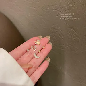 Macro view of dainty moon and star crystal stud earrings with gold finish on fingertips