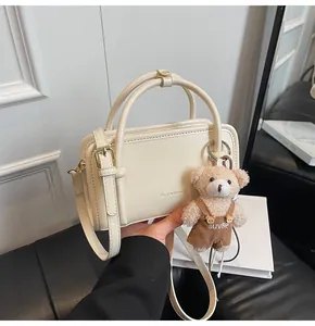 Detail view of cream Boston bag featuring a cute bear charm and embossed logo.