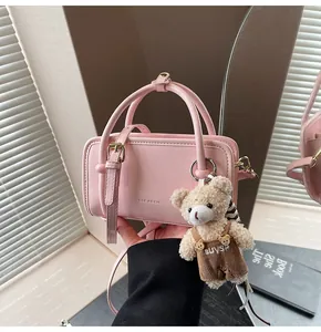 Detailed shot of pink Boston handbag featuring a plush bear charm and embossed brand logo