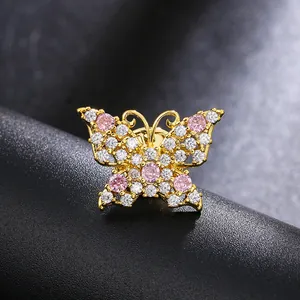 Makro-Detail einer goldenen Schmetterlingsbrosche mit rosa und klaren Steinen auf Leder