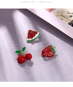 Close-up detail of colorful enamel fruit brooches featuring strawberry and cherry.