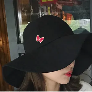 Elegante spilla smaltata a forma di farfalla su un cappello nero a tesa larga.