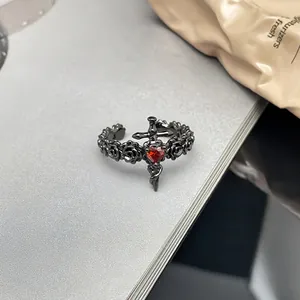 Nahaufnahme eines schwarzen Punk-Rings mit rotem Herzstein und Schwertmotiv im Detail.