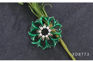 Gedetailleerde close-up van een vintage groene emaille bloemspeld met elegante witte parels.