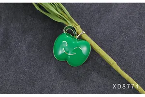Close-up van een groene emaille appelbroche met een lachend gezicht op donkere basis