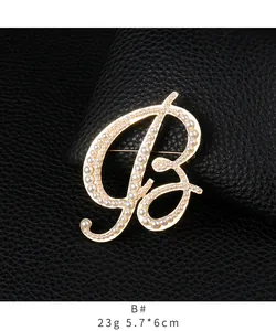 Detail view of a gold-tone letter B brooch with pearl embellishments on leather.