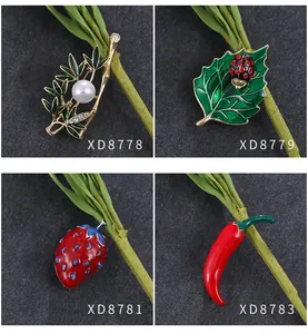 Gedetailleerde collage met emaille broches in de vormen bamboe, lieveheersbeestje, aardbei en chili.