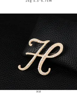 Detail view of a gold-plated letter H brooch with elegant pearl embellishments.