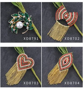 Vier elegante metalen broches met parelbladontwerp en rode straskwastjes.