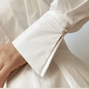 Detail view of a sew-free pearl button used as a decorative cufflink on a white shirt.