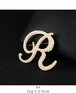 Macro detail of elegant gold letter R brooch adorned with shimmering white pearls