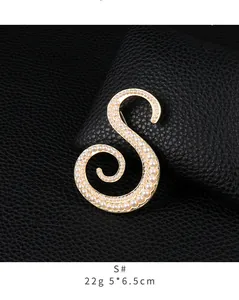 Close-up detail of a golden pearl-encrusted letter S brooch with 5x6.5cm dimensions