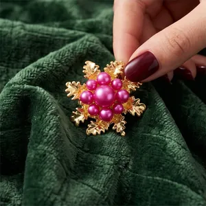 Elegant gold floral camellia brooch with vibrant pink pearls on green textured fabric background.