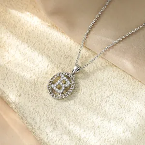 Primo piano del ciondolo lettera B in argento con zirconi su sfondo di seta pregiata.