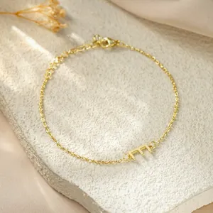 Detail shot of a dainty gold-plated titanium steel chain bracelet with a letter E charm.