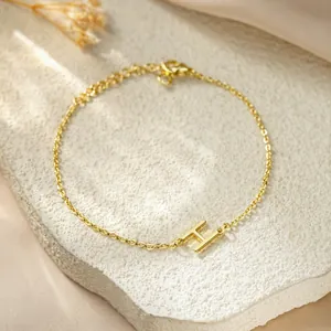 Macro detail of a minimalist gold titanium steel chain bracelet with a letter H charm