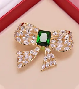 Elegant gold-tone bow brooch featuring a large emerald green stone and zircon accents