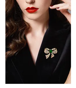 Detail of elegant gold bow brooch with emerald green zircon on a black velvet blazer