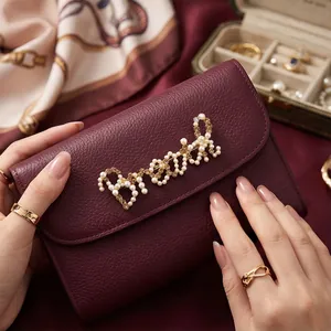 Elegante Perlen-Bonjour-Buchstaben-Brosche an einer luxuriösen weinroten Lederhandtasche.