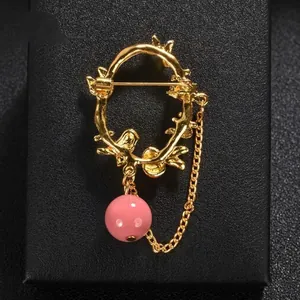 Elegant gold wreath chain brooch featuring a delicate pink bead dangle and metallic chain