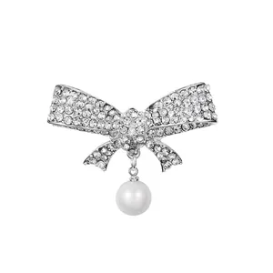 Elegant bow-shaped brooch with sparkling rhinestones and a white pearl drop on white background.