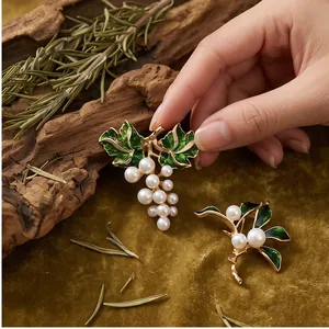 Elegant grape and leaf shaped pearl brooches with green enamel details on a rustic background