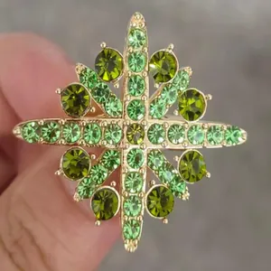 Close-up of elegant snowflake brooch with vibrant green crystals in gold setting