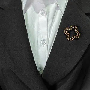 Eleganter goldener Kleeblatt-Anstecker mit schwarzen Strasssteinen auf einem schwarzen Blazer.