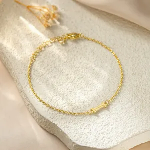 Close-up of golden titanium steel bracelet with letter I charm on textured white stone