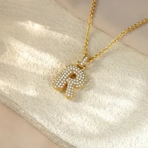 Macro view of gold pavé-set lowercase letter r pendant with clear crystals