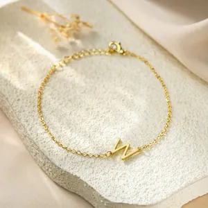 Detailed macro view of a gold titanium steel bracelet featuring a letter W charm