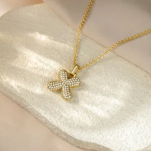 Detailed view of an iced-out gold bubble letter X pendant necklace on a textured stone