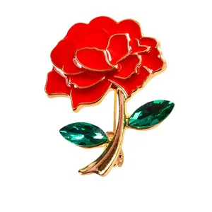 Elegant red rose brooch with green crystals and gold-tone stem on white background