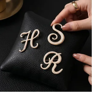 Elegant vintage-style pearl-encrusted English letter brooches on black cushion background