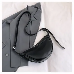 Detailansicht einer schwarzen Halbmond-Tasche aus Kunstleder auf einem grauen Blazer.