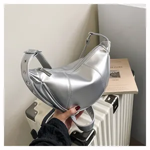 Nahaufnahme einer metallisch silbernen Halbmodetasche auf einem weißen Koffer