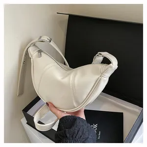Cremeweiße Mondsichel-Schultertasche aus Leder in der Hand mit schwarzer Geschenkbox