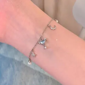 Close-up of a delicate silver charm bracelet featuring pearl heart and moon motifs
