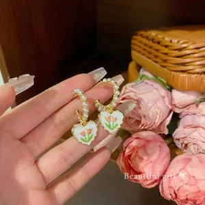 Close-up of vintage heart earrings with pearls and tulip pattern held by hand